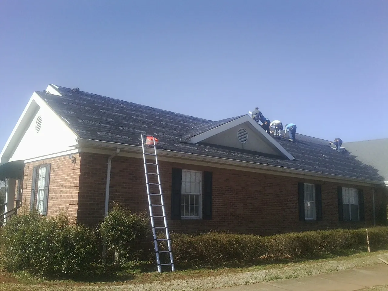 Crew tearing shingles off a brick ranch roof with a ladder set — Metal Roof Repair work by our crew in New Cambria