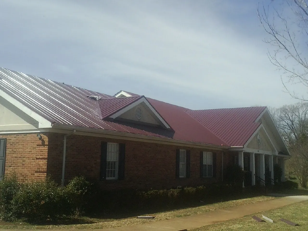 Red metal roof with gabled entries on a long brick building, from a Hail Damage Roof Repair job in New Cambria