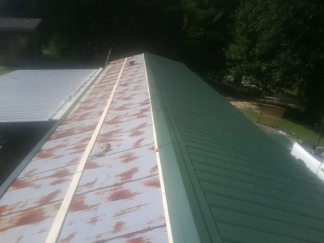 Old rusted panels beside newly installed green metal roofing — Wind Damage Roof Repair by Roofing Brothers in New Cambria