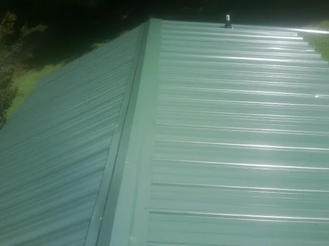 New green metal panels meeting at the ridge of a roof — Flat Roof Repair work by our crew in New Cambria