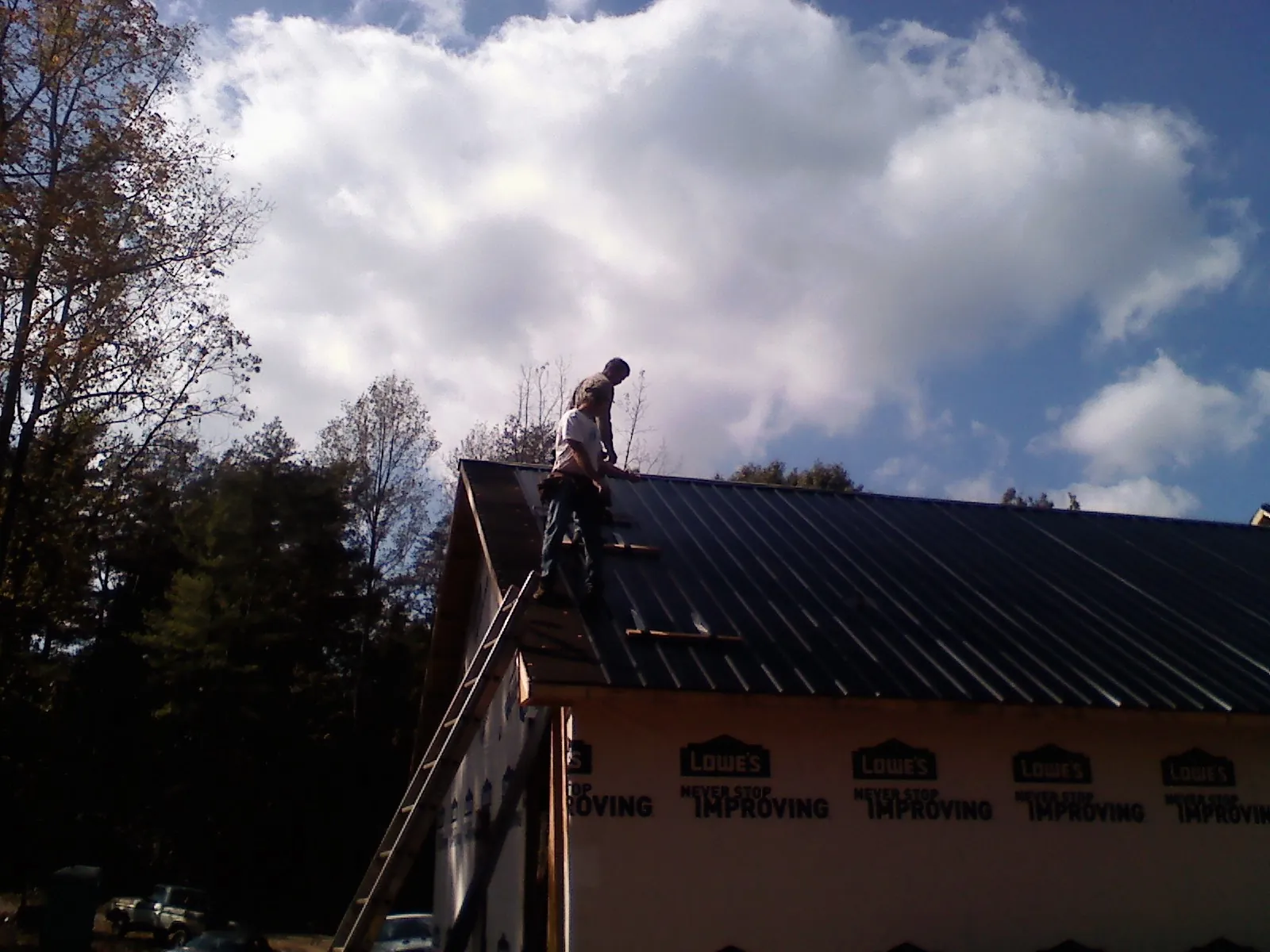 Roofer fastening dark metal panels high against a cloudy sky, from a Roof Inspection job in New Cambria