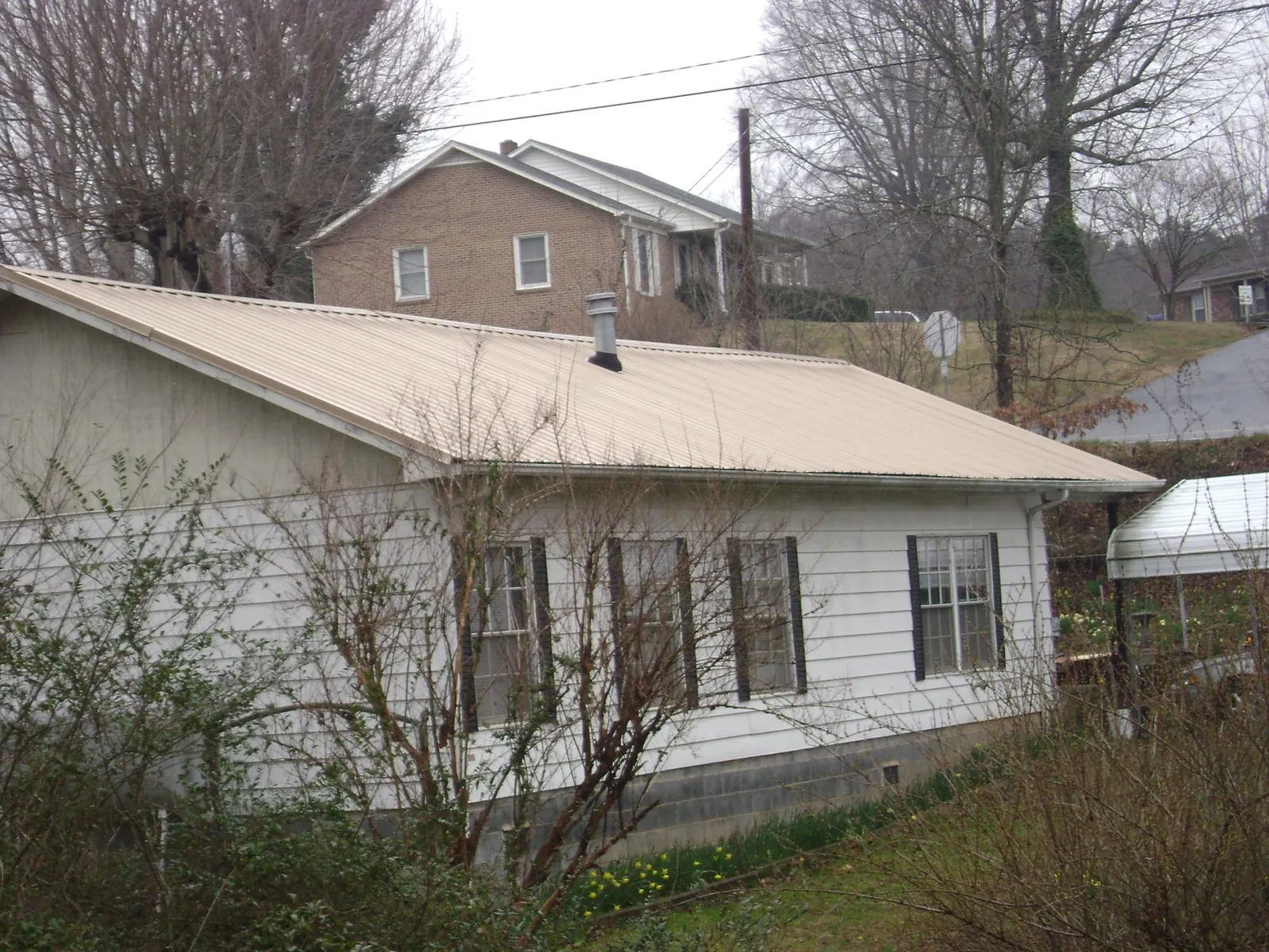 Tan metal roof on a white sided house set into a hillside — Commercial Roofing by Roofing Brothers in New Cambria